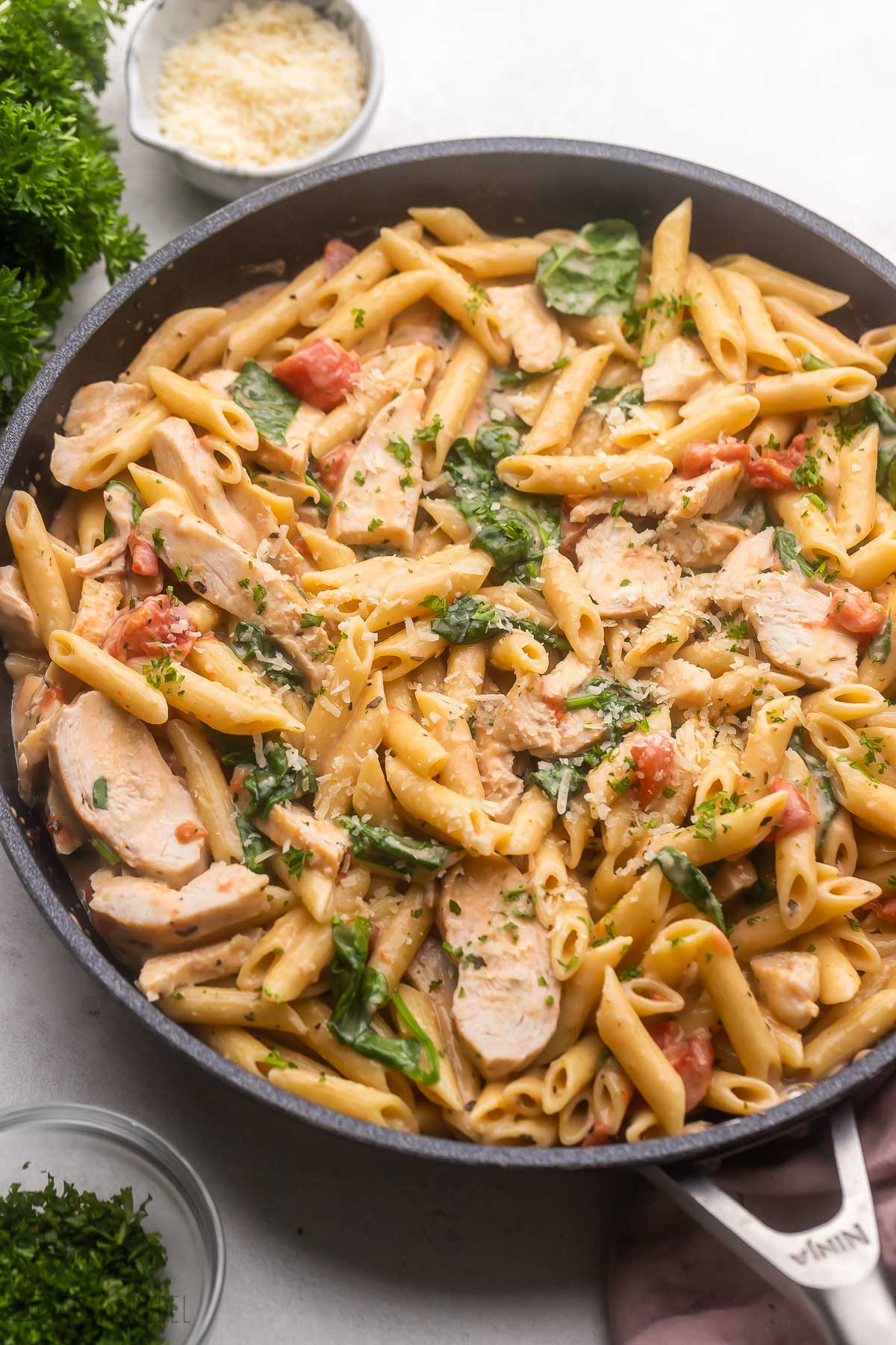 a large pan of chicken penne pasta topped with parmesan.