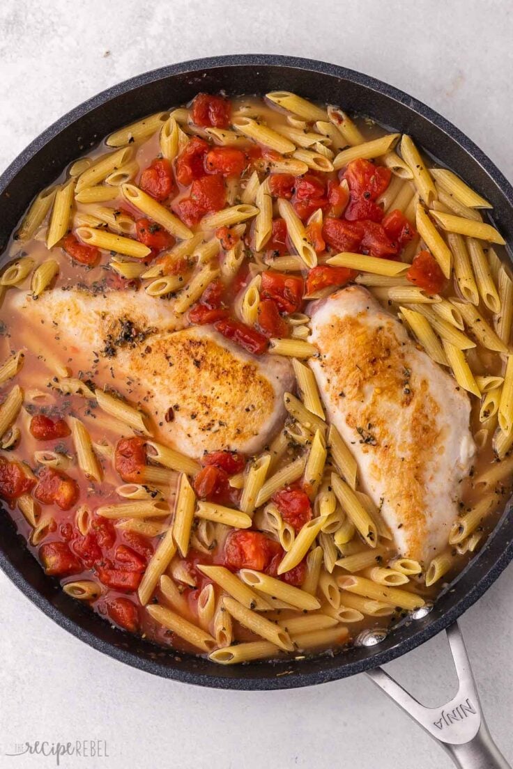 black pan on grey surface filled with chicken penne pasta.