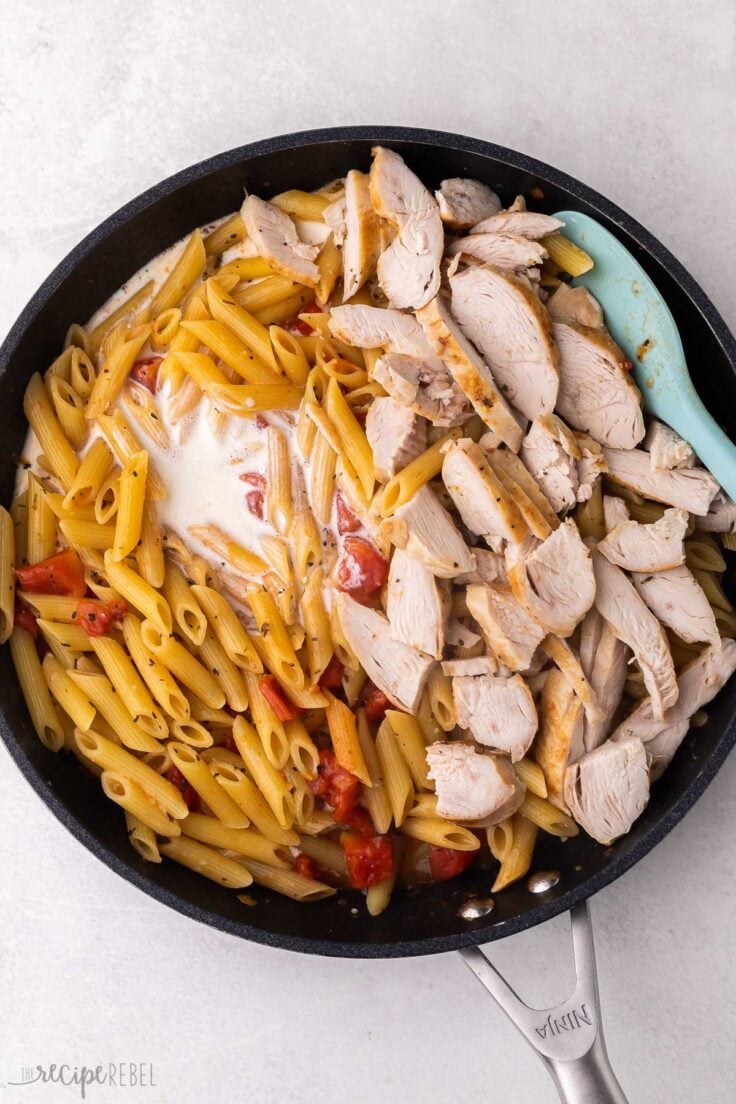 large pan filled with chicken penne pasta and blue spatula.
