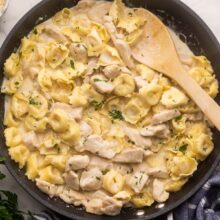 large black pan filled with chicken tortellini alfredo and wooden ladle.