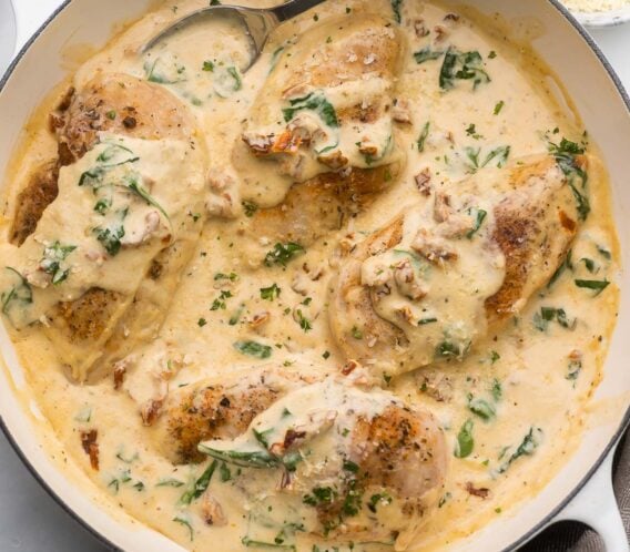 large white pan full of creamy tuscan chicken and a spoon.