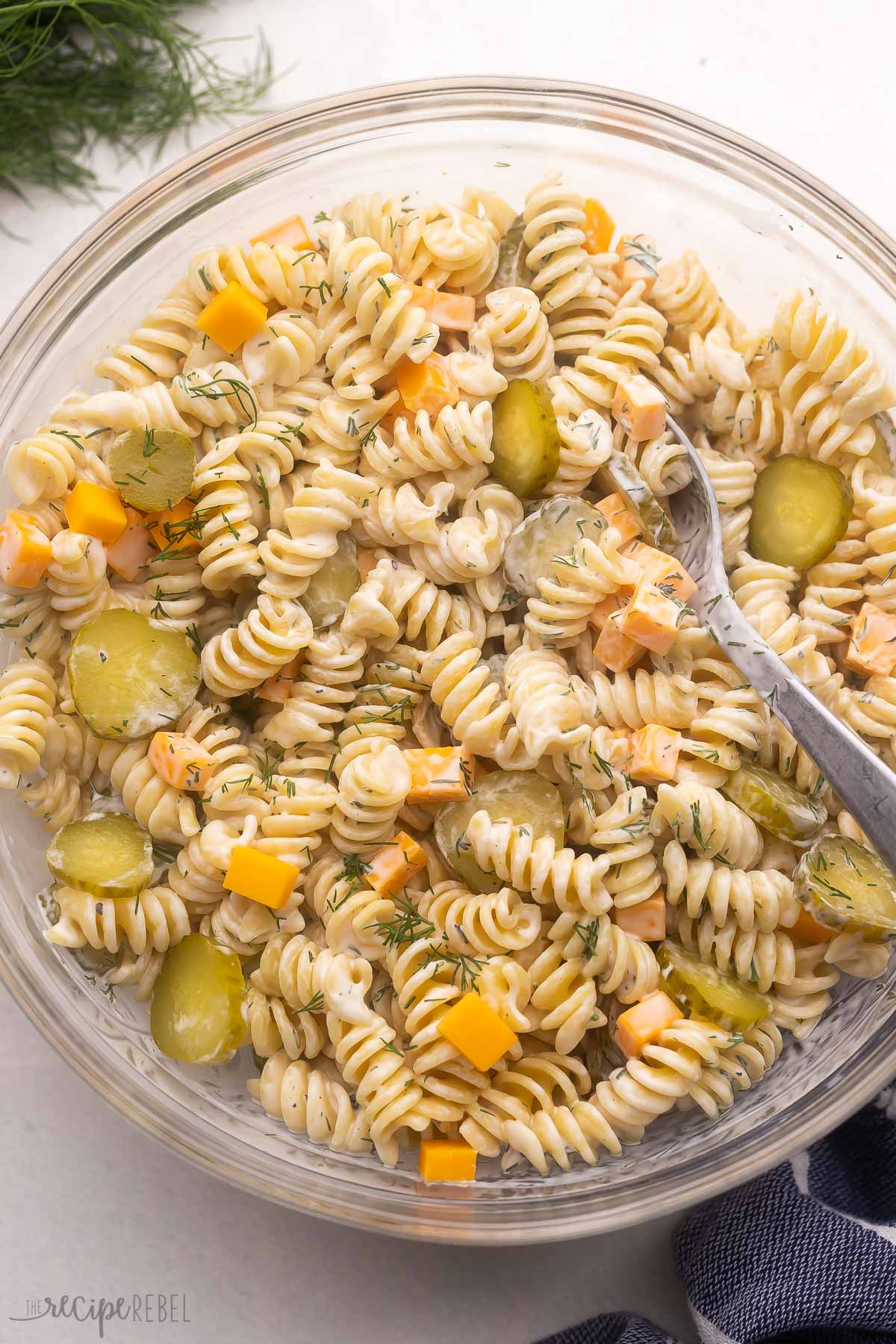 large glass bowl filled with dill pickle pasta salad and spoon.