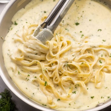 tongs grabbing pasta out of pan of easy alfredo sauce.