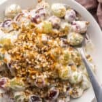 spoon scooping grape salad out of a white bowl.
