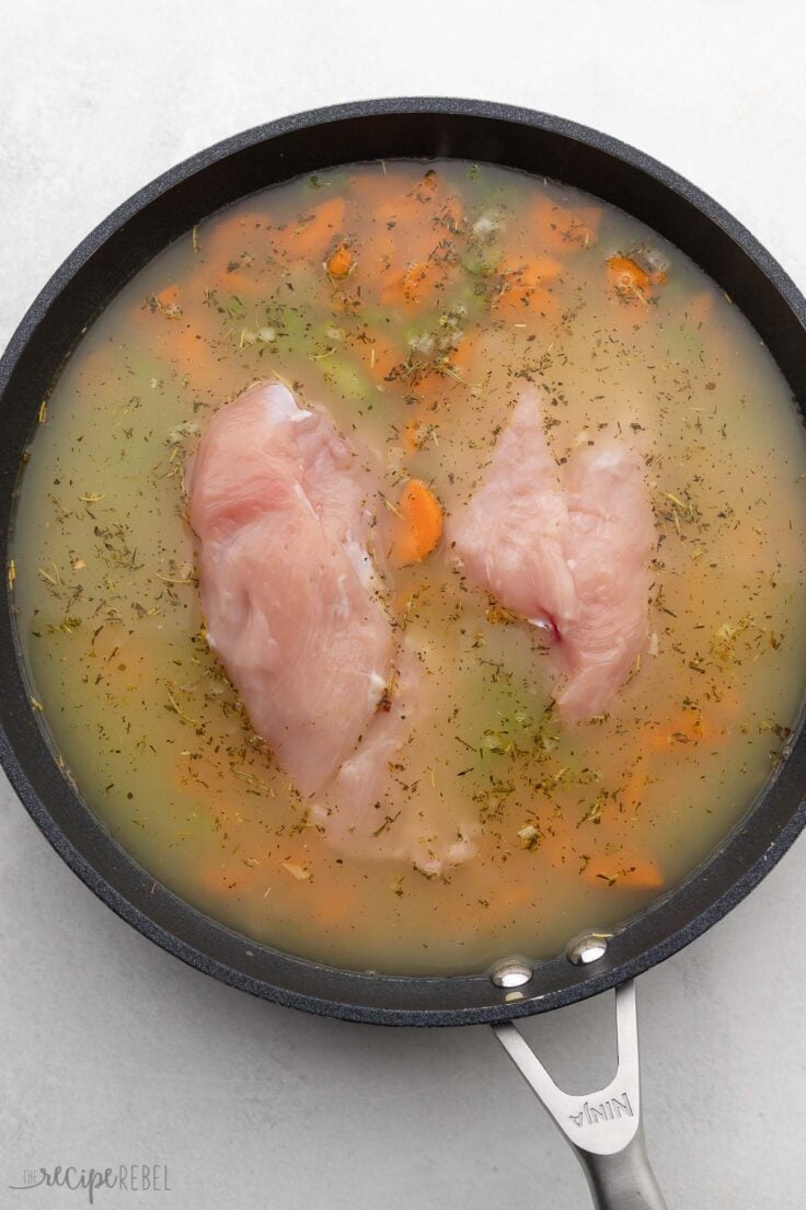 chicken breasts and broth added to black frying pan.