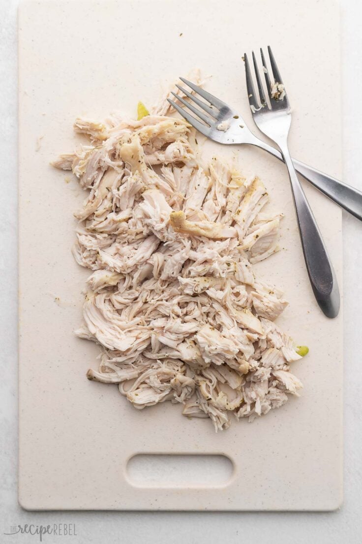 white cutting board with shredded chicken and forks on it.
