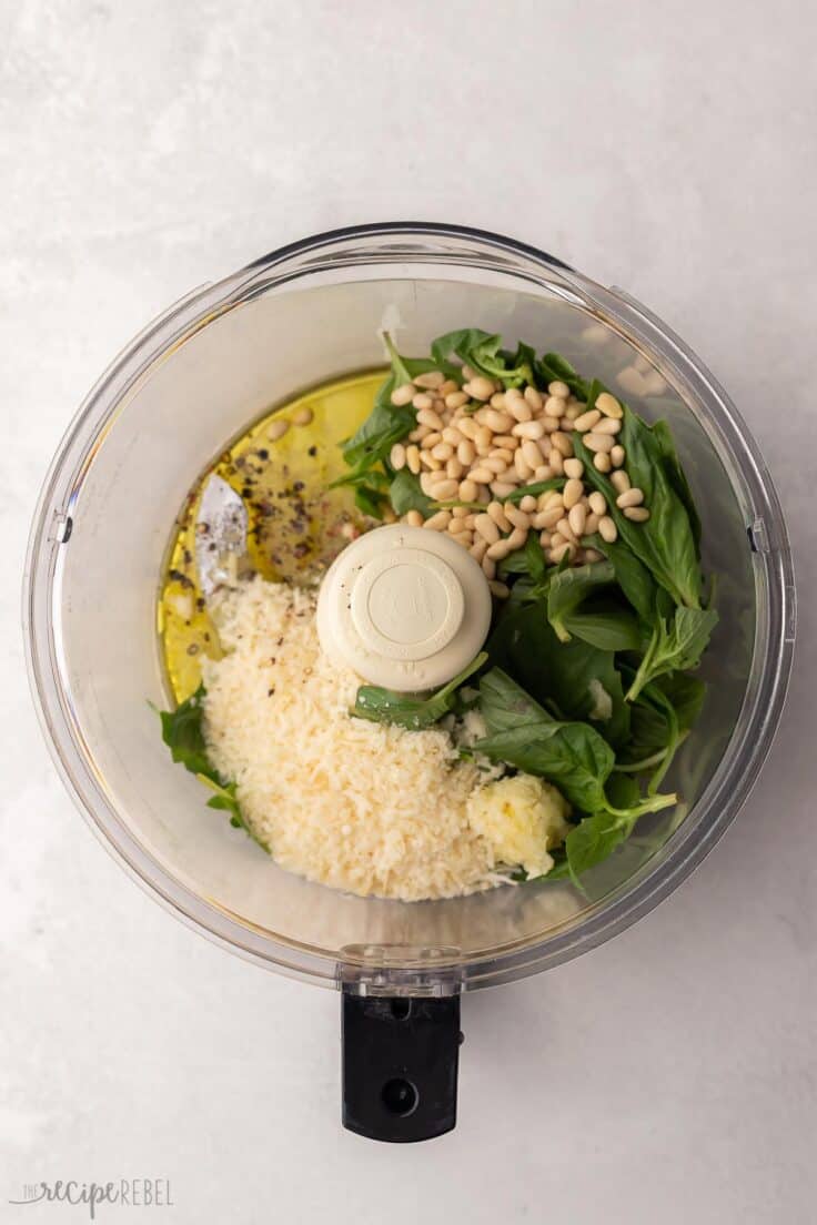 food processor filled with pesto ingredients on grey surface.