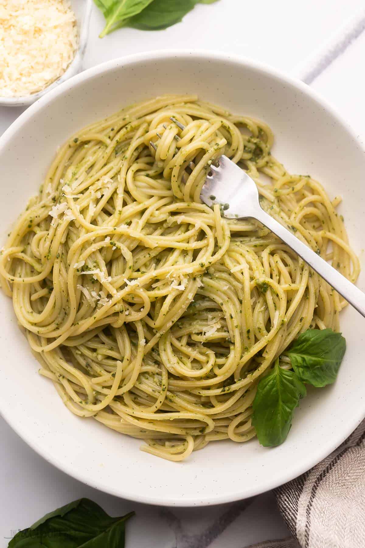 white plate full of pesto pasta and a fork.