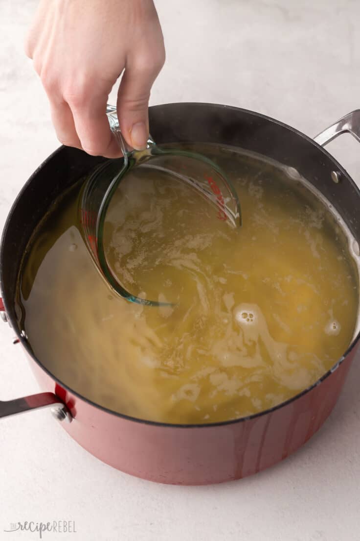 measuring cup scooping pasta water out of a large bowl of cooked pasta.