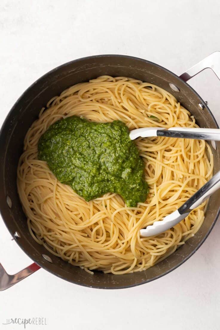 pesto added to top of large pot of cooked pasta.