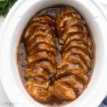 sliced pork tenderloin covered in glaze in a white slow cooker.