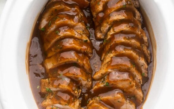 sliced pork tenderloin covered in glaze in a white slow cooker.