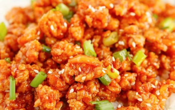 A serving of orange ground chicken is garnished with green onions.