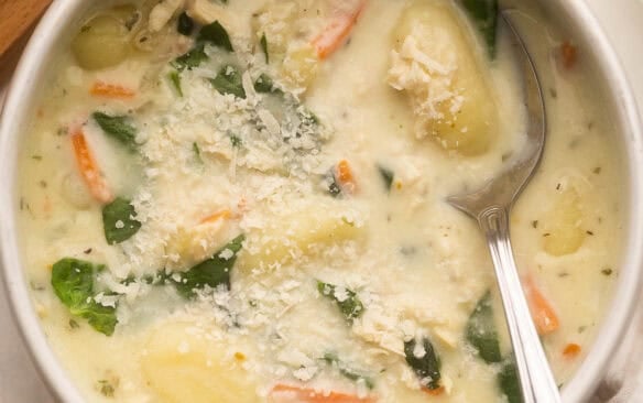 square image of chicken gnocchi soup in a bowl with a spoon.