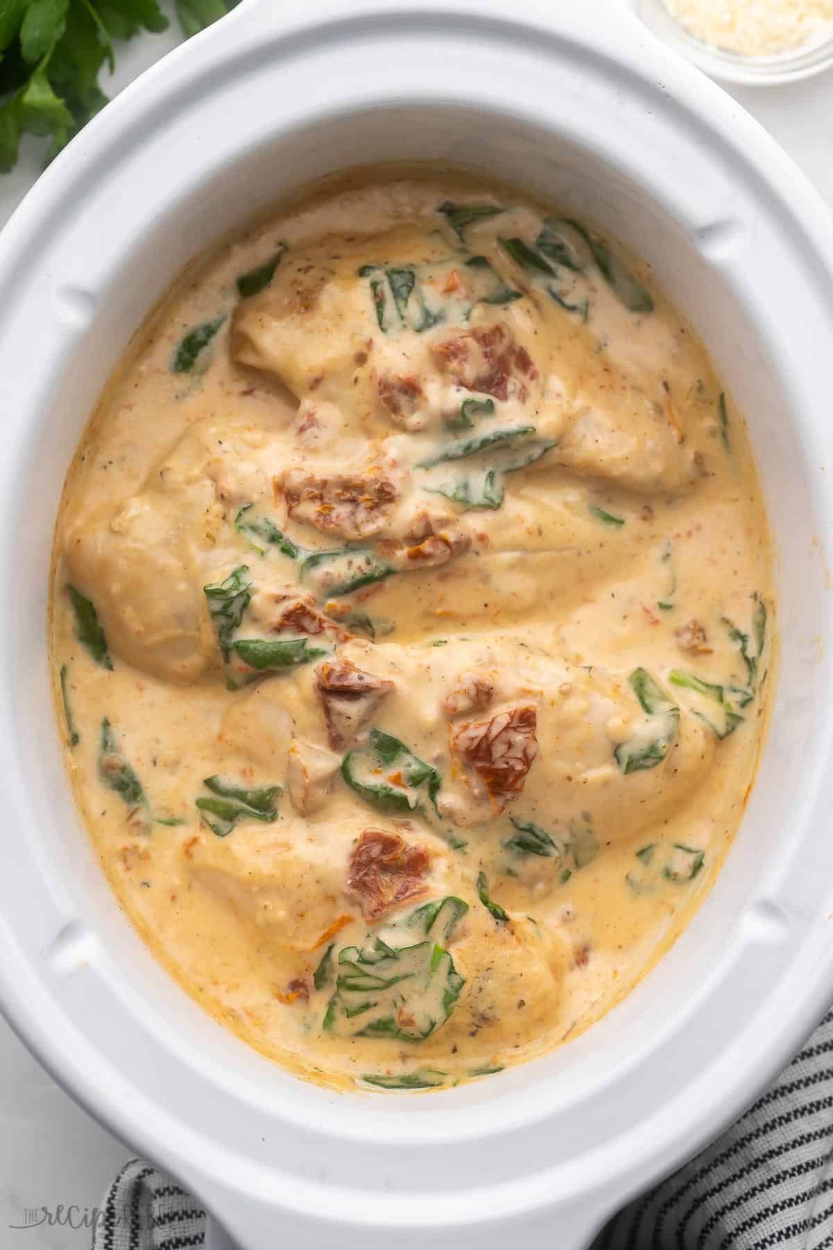 overhead view of a white crockpot with cooked tuscan chicken inside.