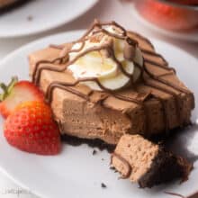 white plate with a nutella cheesecake bar drizzled with chocolate and strawberries beside.