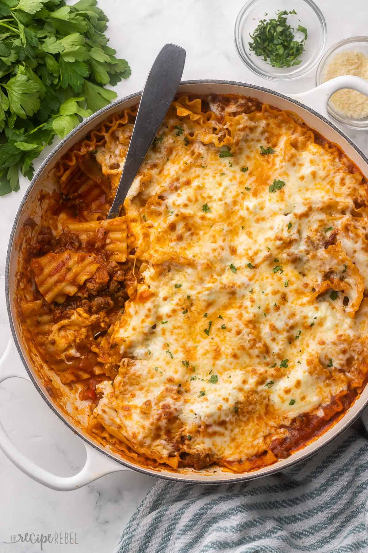 This one pan Skillet Lasagna Recipe comes together in just 30 minutes - it's the easiest lasagna you'll ever make! Italian sausage, tomato sauce, pasta and loads of cheese are featured in this simple stove top recipe. #recipe #dinner #pasta | easy dinner recipes | dinner ideas | one pot pasta | one pan dinner | ground beef | italian sausage | easy lasagna | family meals large skillet of skillet lasagna with parsley beside.