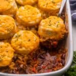 white pan of chili cheese casserole with a biscuit being scooped out.
