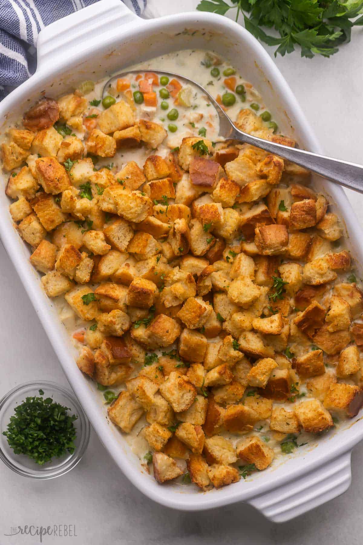 chicken and stuffing casserole in white baking dish with metal spoon scooping.