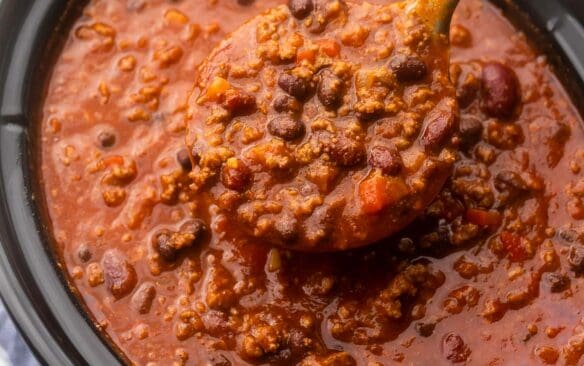 steel ladle scooping chili out of black crockpot.