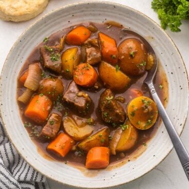 close up of a speckled bowl filled with beef stew and a spoon in it.