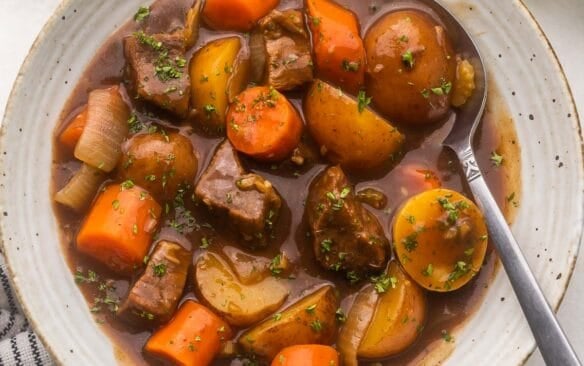 close up of a speckled bowl filled with beef stew and a spoon in it.