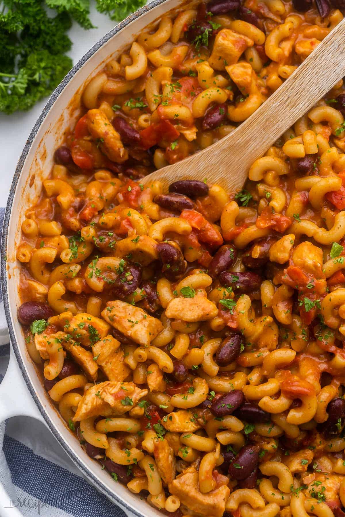 large white dish filled with bbq chicken chili mac and a wooden ladle.