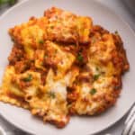 close up of ravioli lasagna on a plate topped with chopped parsley.