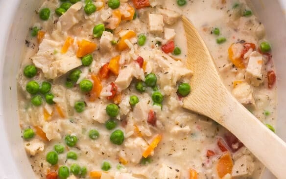 a wooden ladle inside a slow cooker filled with chicken and rice.