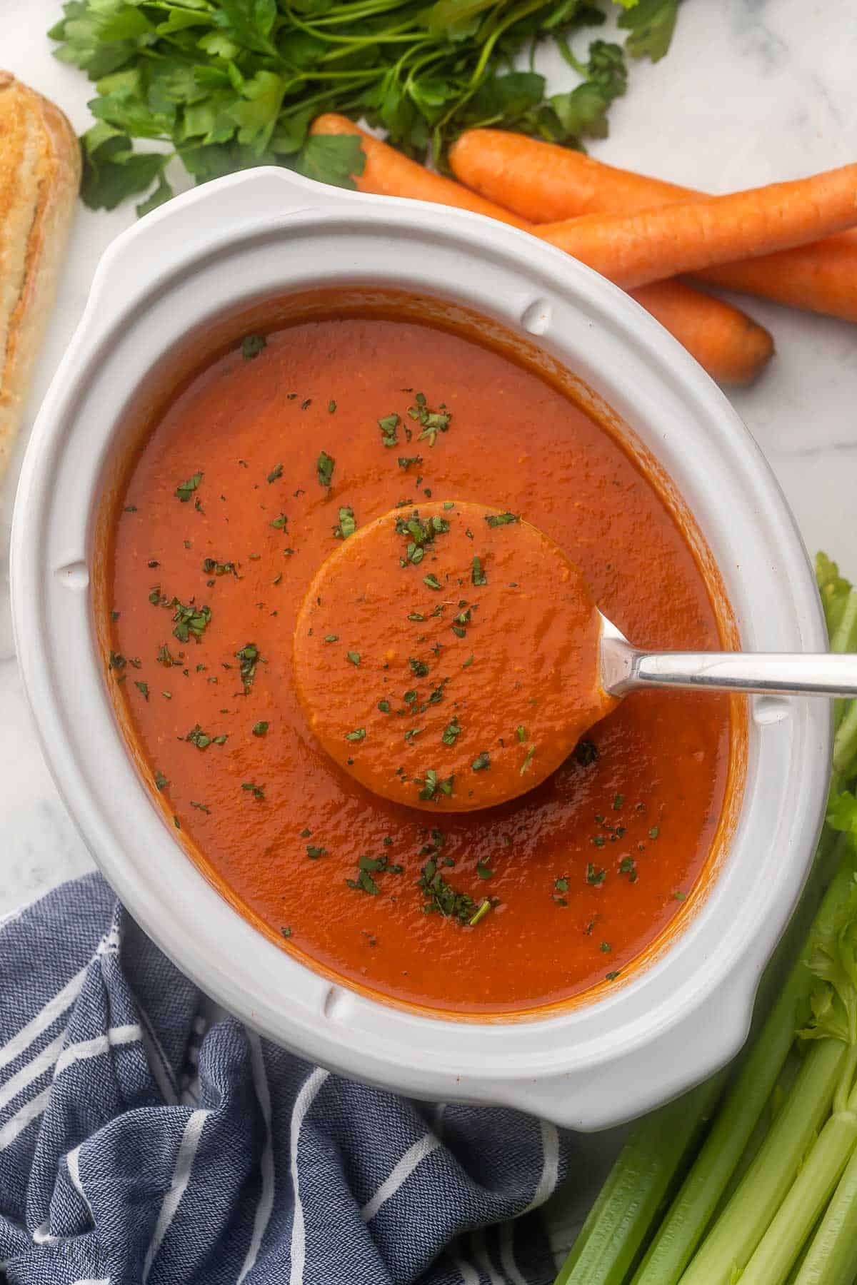 steel ladle scooping creamy tomato soup out of white slow cooker.