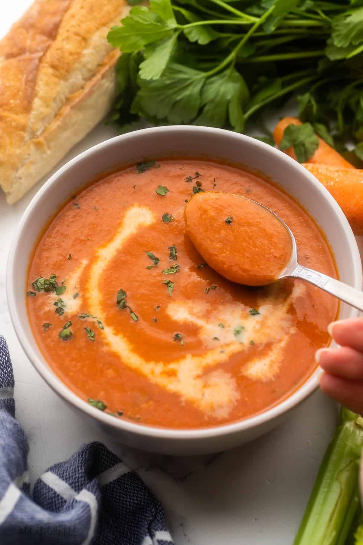 a spoonful of tomato soup above bowl with bread beside.