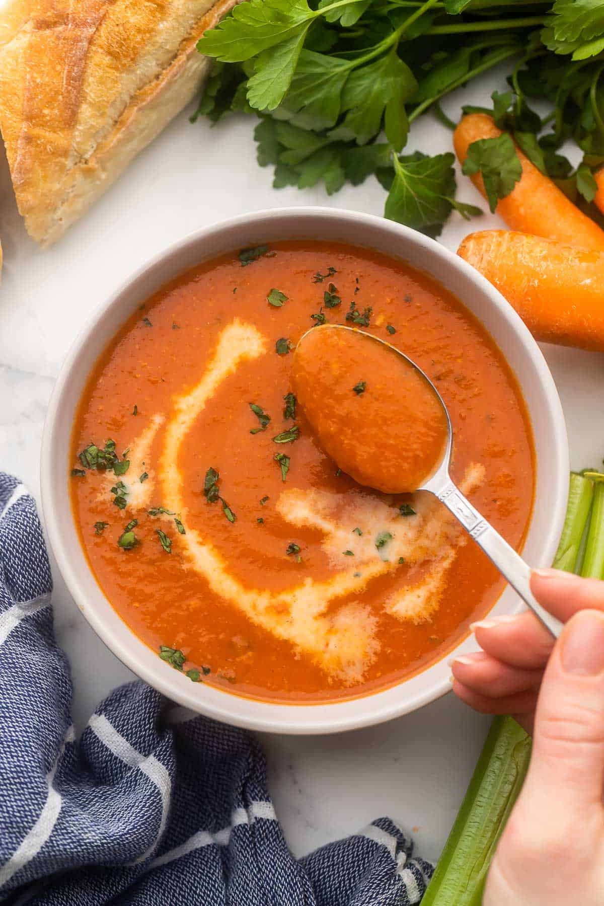 Slow Cooker Creamy Tomato Soup (with hidden veggies) is the best way to sneak some nutrients into the bowl of any picky eater. This flavorful, creamy tomato soup secretly features lots of carrots and celery. #recipe #dinner #soup | soup recipes | easy dinner | healthy soup | tomato soup | slow cooker soup | slow cooker recipes | easy dinner ideas scooping creamy tomato soup out of bowl.