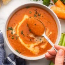 close up of a spoon scooping creamy tomato soup out of bowl.