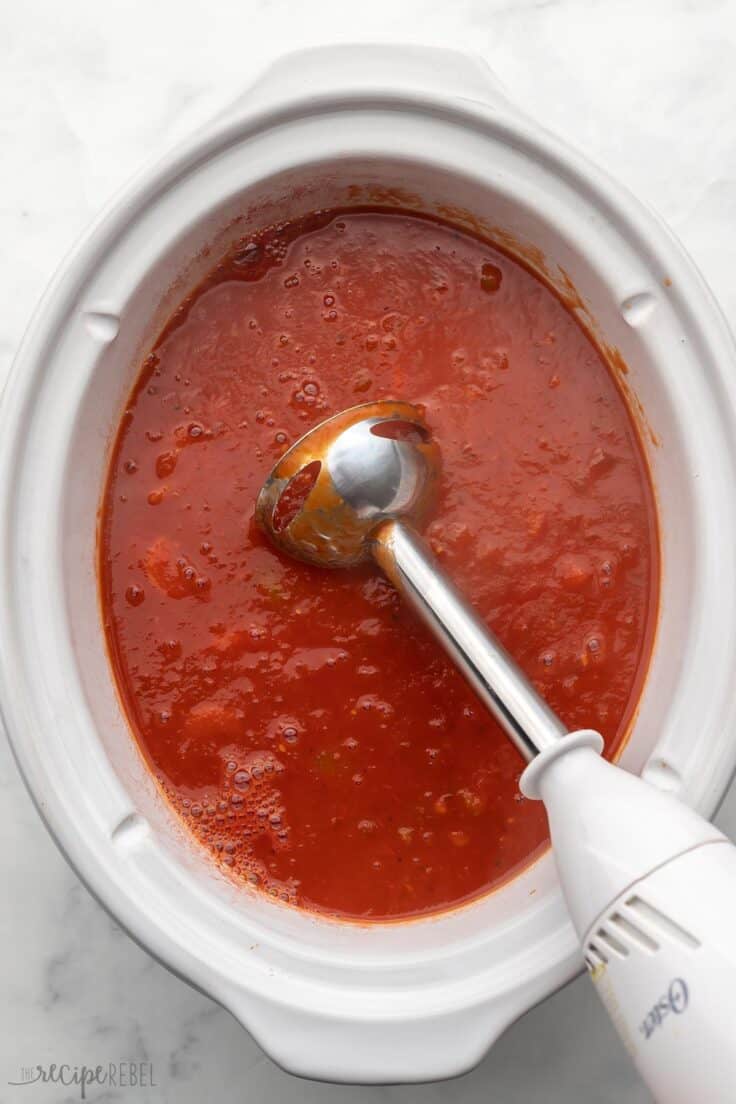 immersion blender in white slow cooker filled with soup.