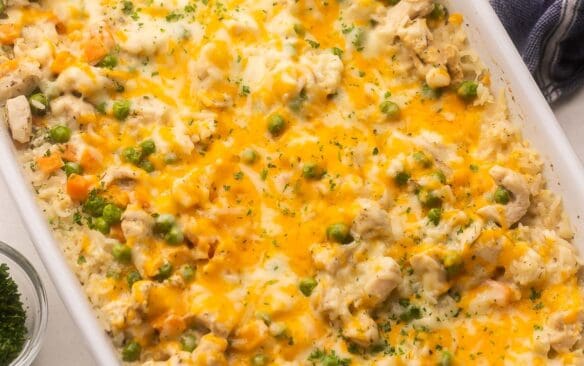 white baking dish full of chicken and rice casserole with chopped parsley beside.