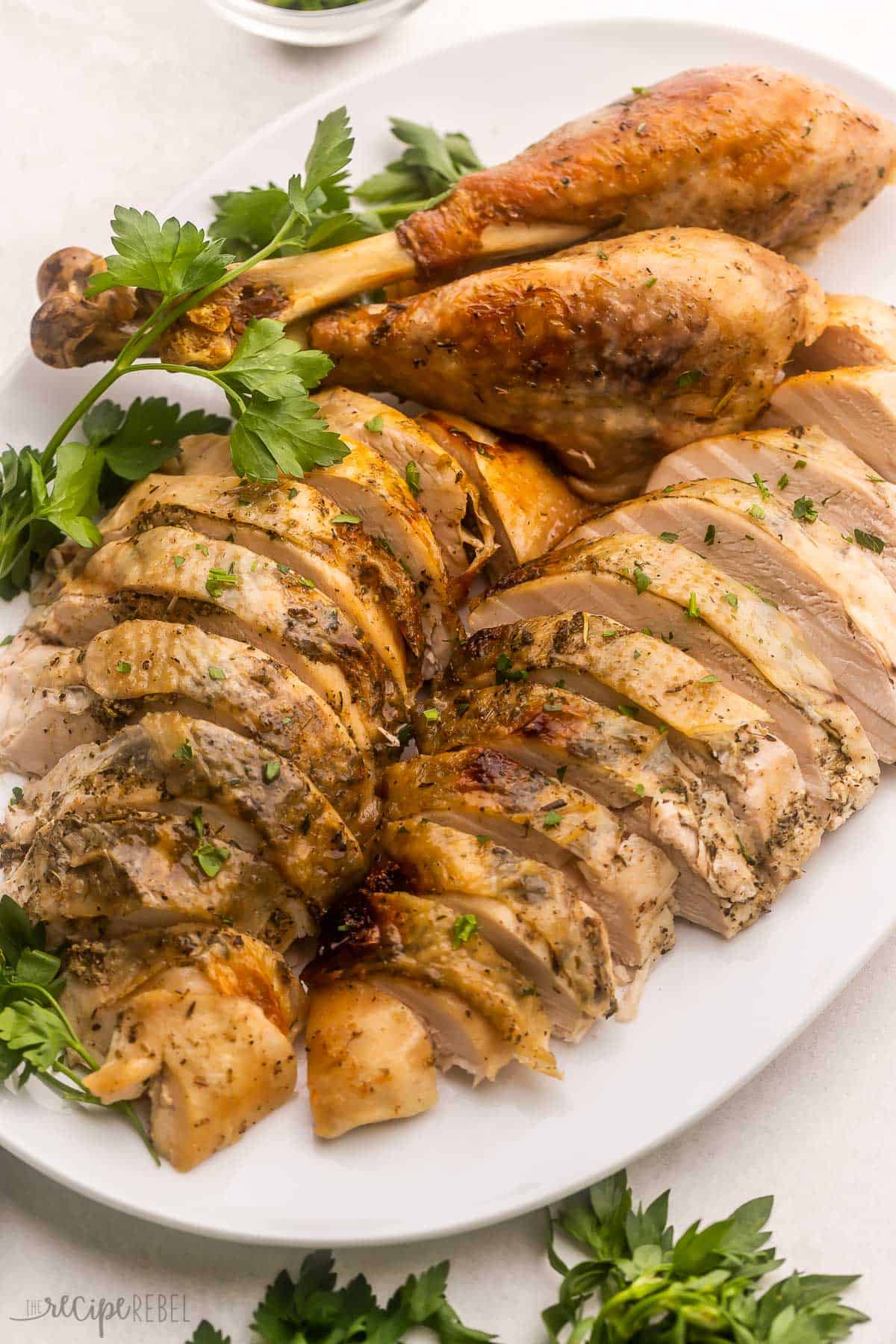 white platter filled with sliced turkey and parsley beside.