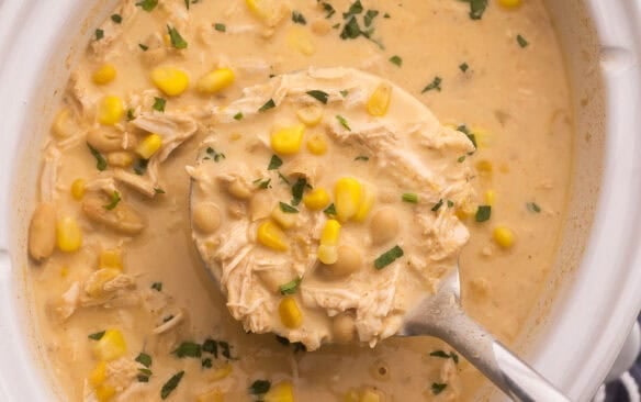 white chicken chili being scooped out of white crockpot.
