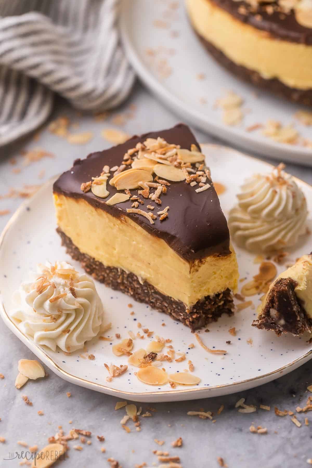 white plate with a piece of nanaimo bar cheesecake with whipped cream and coconut beside.