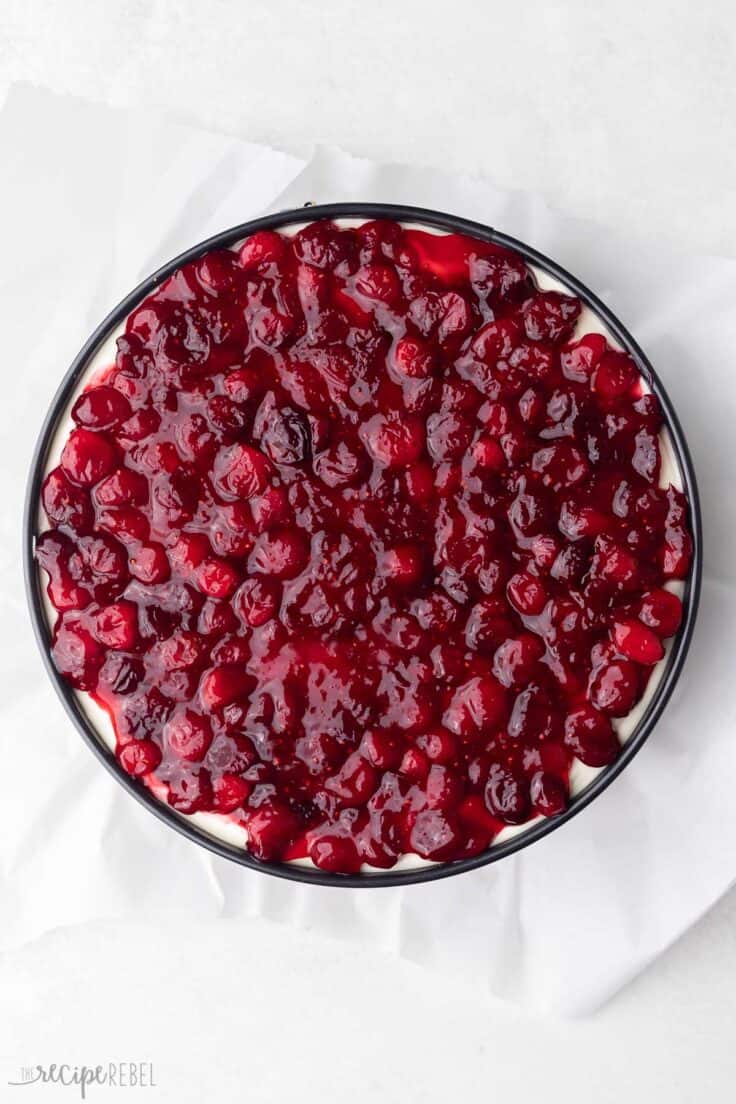 cranberries spread on top of cheesecake in pan.