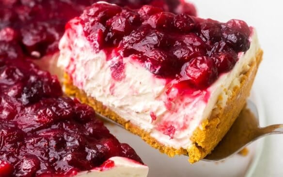 a piece of white chocolate cranberry cheesecake being lifted off of a plate.