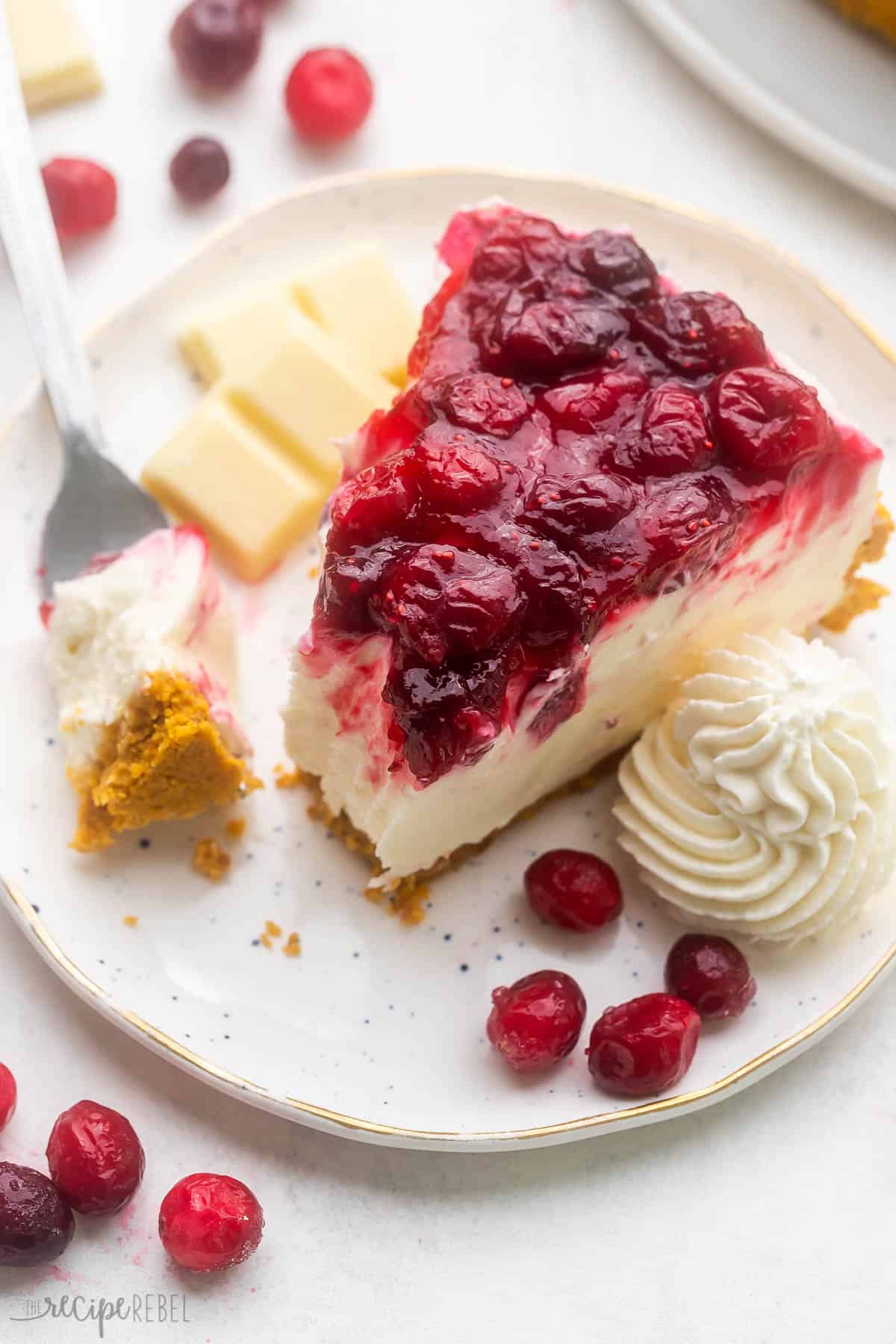 a piece of cheesecake in a plate with whipped cream and cranberries beside.