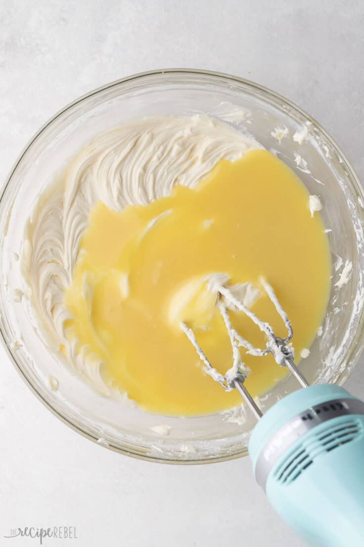 glass mixing bowl with melted white chocolate added to the top of cream cheese mixture.