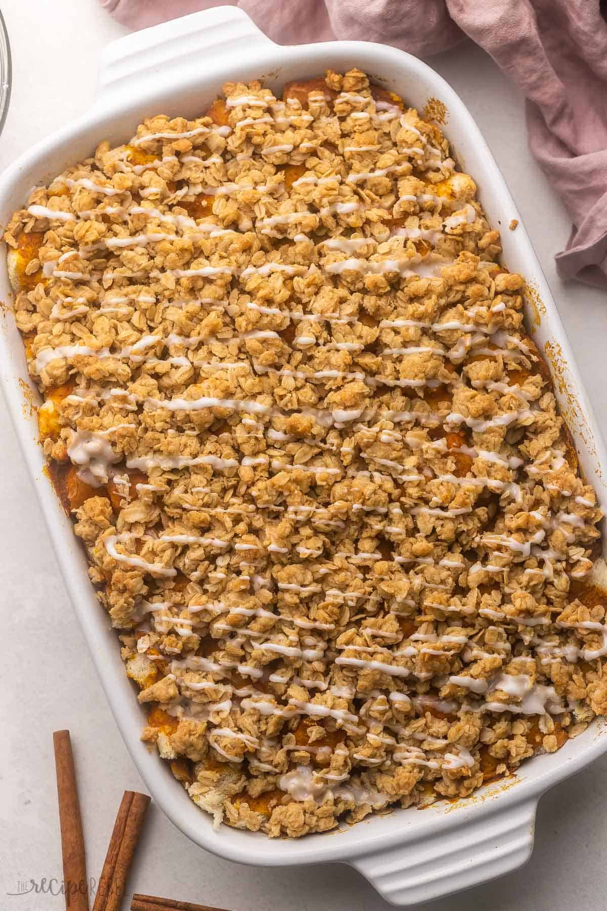 a full pan of pumpkin french toast casserole with glaze on top and cinnamon sticks beside.