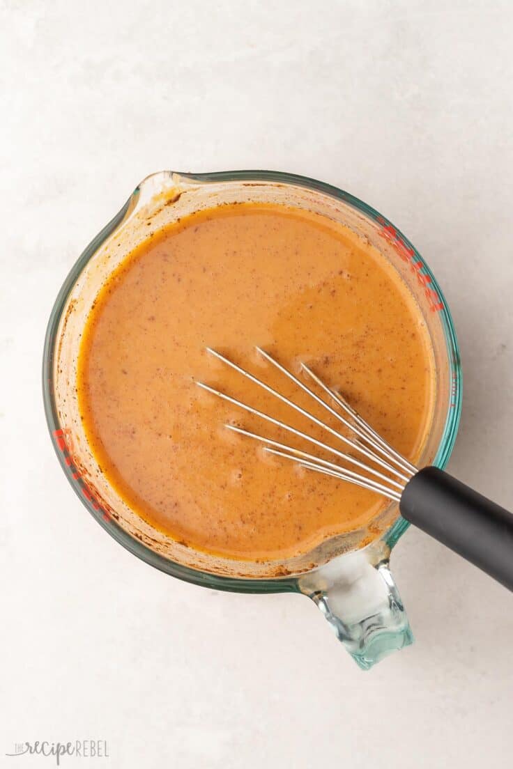 glass measuring cup full of mixed pumpkin ingredients and whisk.