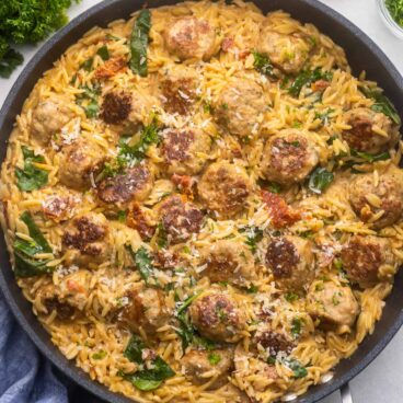 square image of marry me chicken meatballs with orzo in a black pan.