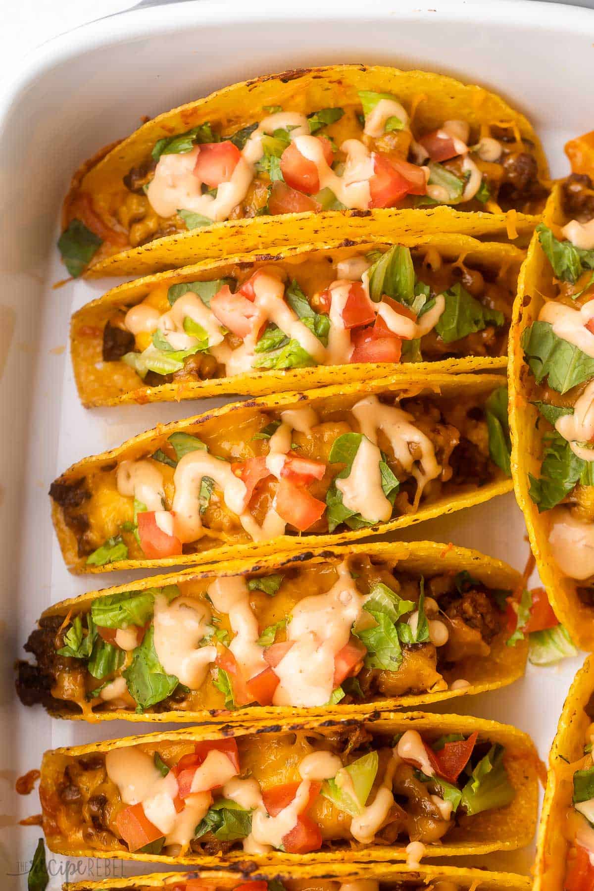 These Cheeseburger Baked Tacos are filled with barbecue ground beef and cheddar cheese and topped with all your favorite burger toppings! It's an easy dinner recipe that's great for prepping ahead. #groundbeef #dinner #recipe | ground beef recipes | taco recipe | make ahead meal | easy dinner ideas | dinner recipes | bbq | barbecue sauce | cheeseburger recipes baked bbq cheeseburger tacos in a baking dish.