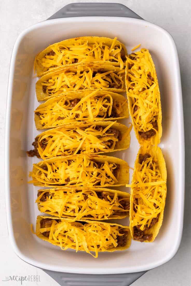 tacos topped with shredded cheese inside a white baking dish.