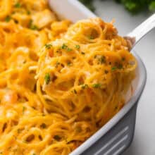 a scoop of chicken spaghetti bake coming out of the pan with chopped parsley on top.