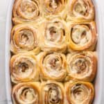 a white pan full of of frosted cinnamon buns.