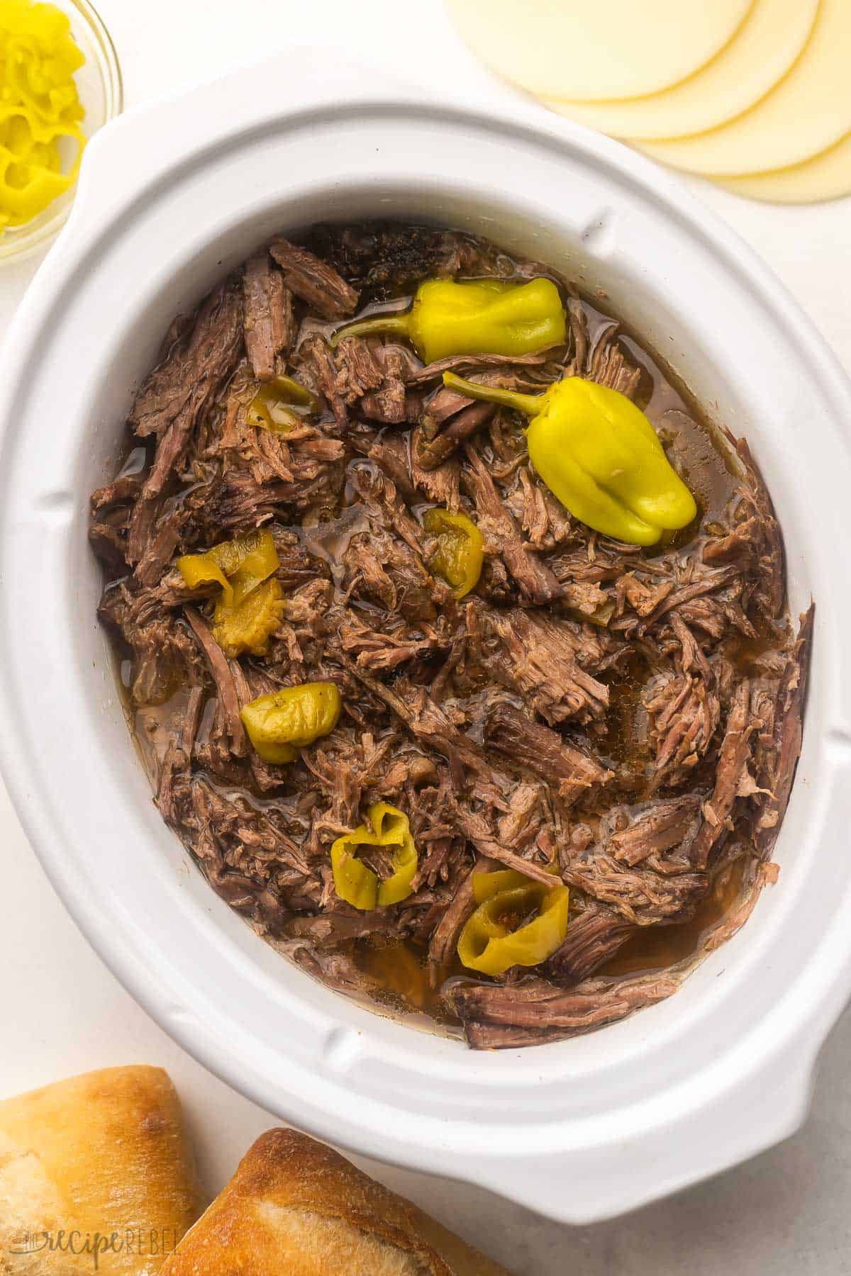 shredded italian beef in crockpot with peppers on top.